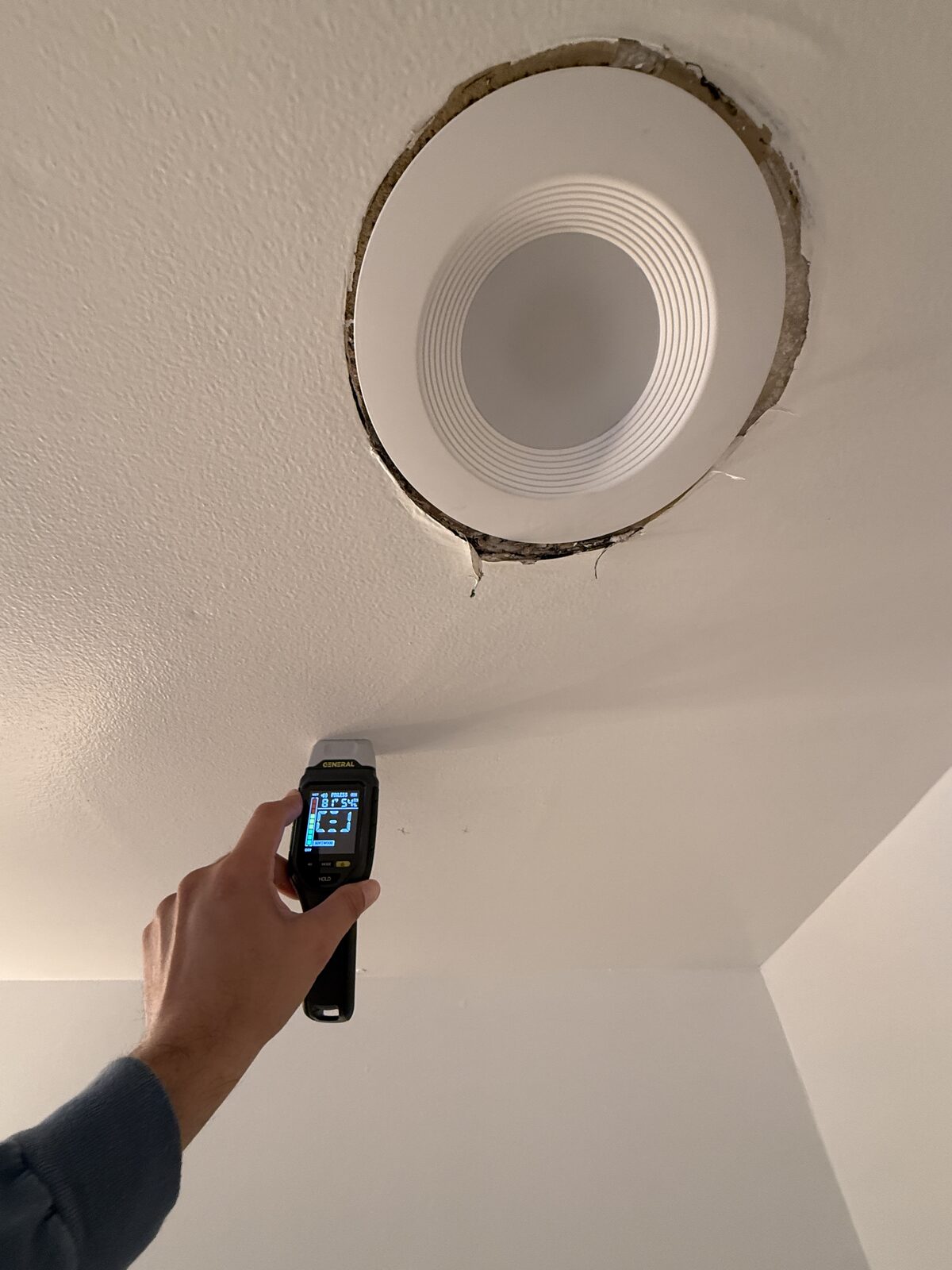 Moisture meter reading a damp bathroom ceiling beside a recessed light in a Parkland home